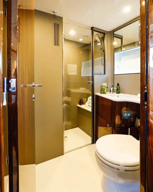 Modern bathroom with a shower cubicle, toilet, sink, and wooden cabinets, featuring toiletries and towels neatly arranged.